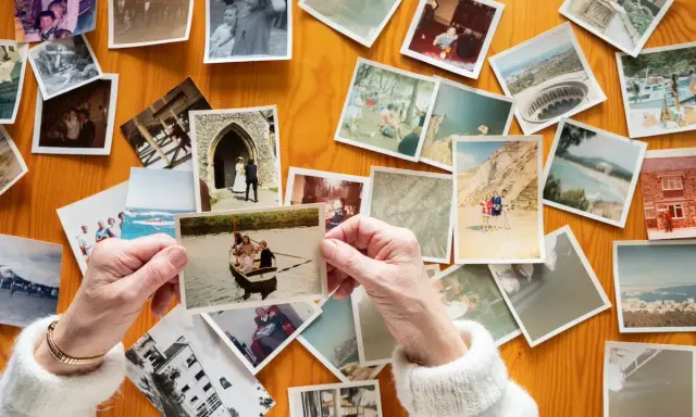 Mani anziane sfogliano vecchie foto stampate su un tavolo di legno, un modo per conservare le foto stampate e i ricordi.