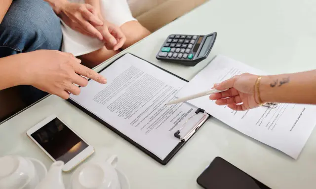 Des mains examinent un contrat de bail verbal, avec un téléphone, une calculatrice et une théière à proximité.
