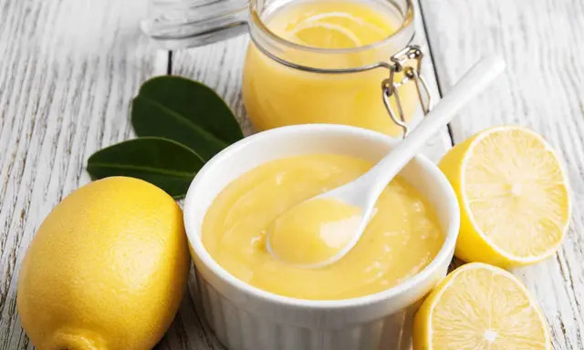 Aksamitny curd cytrynowy w miseczce, obok cytryny i słoiczek z tym pysznym kremem. Idealny do deserów!