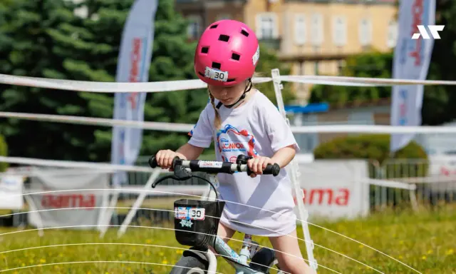 Dziewczynka w różowym kasku na rowerze, z numerem 30. Czy kask na rower dla dziecka jest obowiązkowy? Tak, dla bezpieczeństwa!