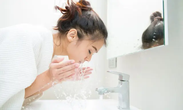 Une jeune femme se lave le visage le matin, sous un jet d'eau fraîche. Une routine beauté essentielle pour se réveiller.