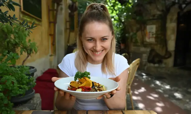 Uśmiechnięta kobieta prezentuje talerz pełen kolorowych warzyw, idealnych na dietę śródziemnomorską.