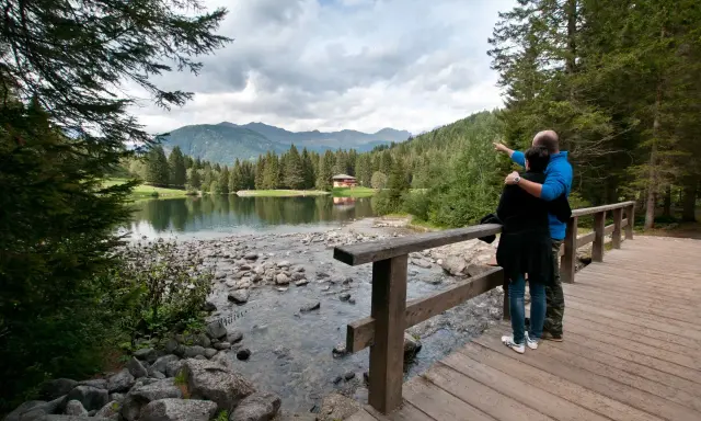 Coppia ammira il lago dei caprioli, con montagne sullo sfondo e una casa tra gli alberi.