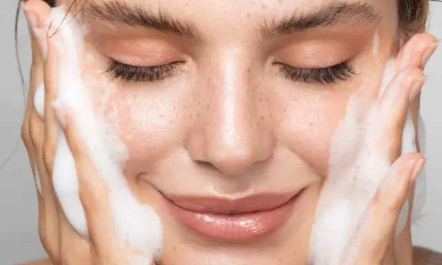 Une femme au visage frais, les yeux fermés, savoure la mousse d'un nettoyant. La définition de la pureté.