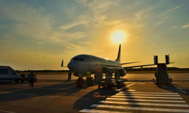 Samolot flydubai na lotnisku o zachodzie słońca. Pracownicy przygotowują bagaż rejestrowany, sprawdzając jego wymiary przed załadunkiem.