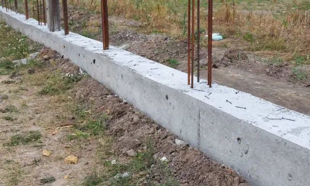 Solidna podmurówka z betonu z wystającymi prętami zbrojeniowymi, gotowa na dalsze prace budowlane.