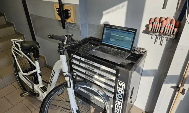 Profesjonalna naprawa rowerów elektrycznych w warsztacie. Biały rower elektryczny, laptop z oprogramowaniem diagnostycznym i zestaw narzędzi.
