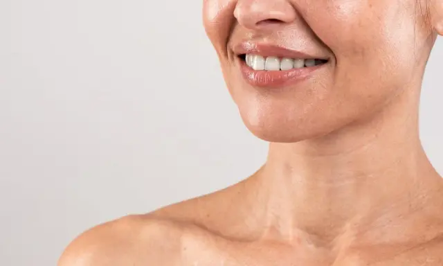 Sorriso radioso con labbra lucide e denti bianchi. La pelle del collo mostra le delicate "collane di Venere", segni di bellezza naturale.