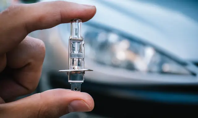 Un dedo sostiene una bombilla de coche, lista para iluminar el camino con sus luces largas.