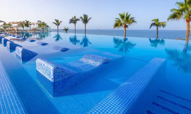 Piscina a sfioro con lettini integrati e palme, vista mare. Un sogno al searesort Riu Gran Canaria.