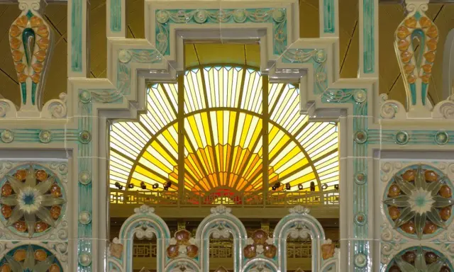 Détails ornementaux en céramique, style art déco, encadrant une verrière jaune rayonnante.