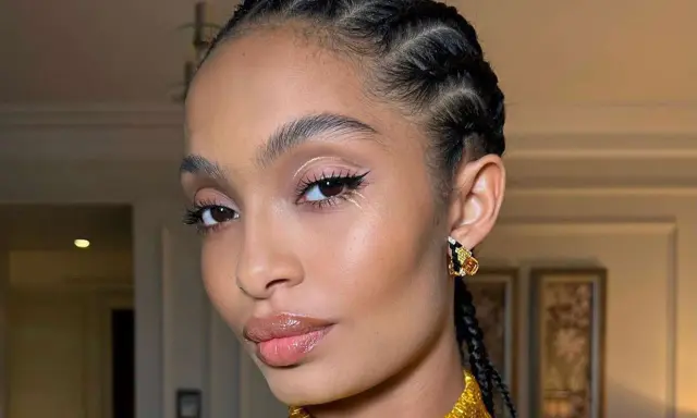 Primer plano de una mujer con trenzas, maquillaje de ojos con delineado y brillo, y labios brillantes.
