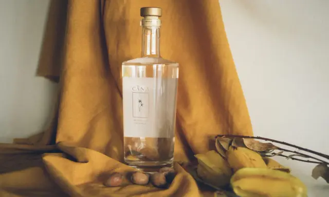 Butelka Cachaça Cãna, brazylijskiego alkoholu z trzciny cukrowej, otoczona owocami i suchymi liśćmi. Cachaca co to? To brazylijski skarb!
