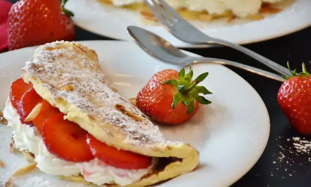 Słodki omlet z bitą śmietaną i truskawkami, posypany cukrem pudrem i płatkami migdałów. Idealny deser na słodko.