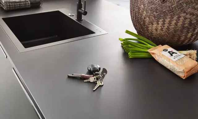 Dunkle Nobilia Arbeitsplatte mit Spüle, Schlüsselbund, Frühlingszwiebeln und Reis. Xtra Arbeitsplatte Nobilia Erfahrung: Praktisch und stilvoll.