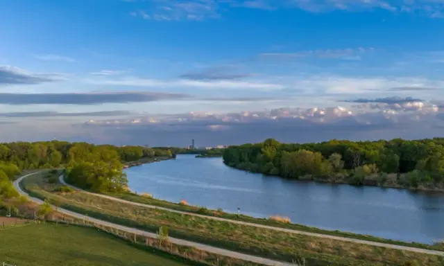 Wisła, jaka rzeka płynie przez Kraków, meandruje wśród zieleni. W oddali widać miejską panoramę.