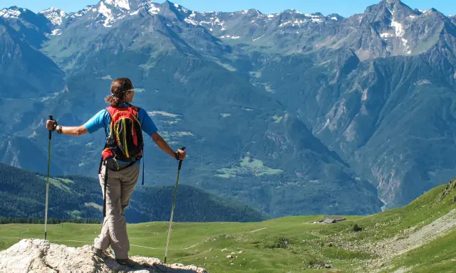 Escursionista con zaino e bastoncini ammira un panorama alpino mozzafiato, perfetto per scoprire gli itinerari della Valle d'Aosta.