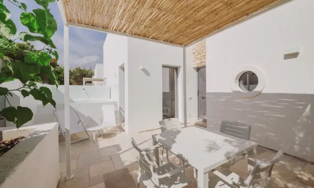 Terrazza con tavolo e sedie bianche, tettoia in bambù, tipica del Nicolaus Club Meditur Village.