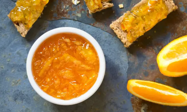 Confiture d'écorce d'orange brillante dans un bol blanc, servie sur des toasts avec des tranches d'orange fraîche.