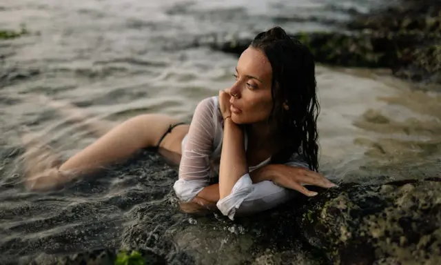 Modella in posa foto artistiche da fare al mare, sdraiata tra le rocce e l'acqua.