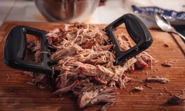 Pulled pork mit Fleischgabel auf Holzbrett. Perfekt für Smoker Rezepte Schwein, z.B. Pulled Pork Sandwiches.