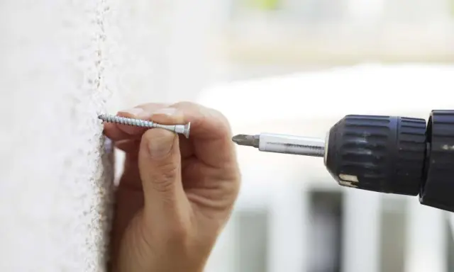 Mano insertando un tornillo en una pared texturizada, útil para saber si una pared es de pladur.