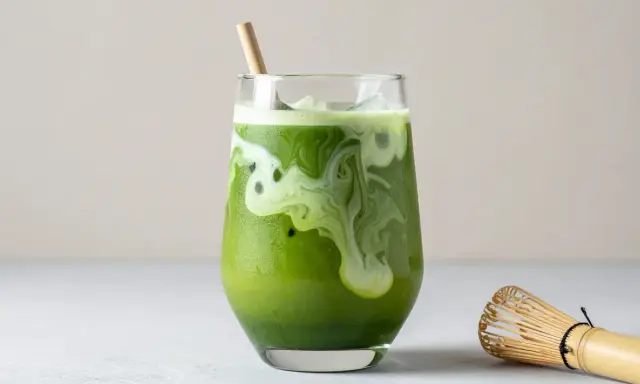 Grönt matcha te med mjölk och is i ett glas, med en bambuvisp bredvid. Tänk på eventuella matcha te biverkningar innan du dricker.