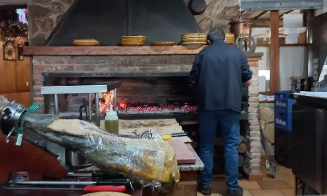 Un hombre trabaja en la cocina del restaurante Emilio Riopar, cerca de un jamonero y un horno de leña.