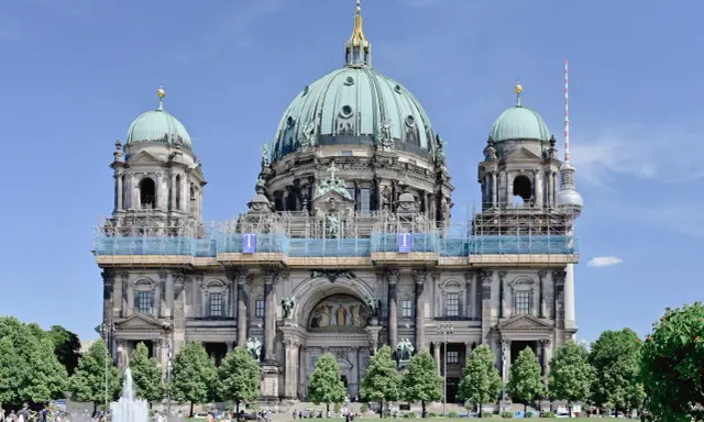 Berlins domkyrka med sina imponerande kupoler är ett måste när man undrar vad ska man se i Berlin. En fontän och grönskande träd ramar in den vackra byggnaden.