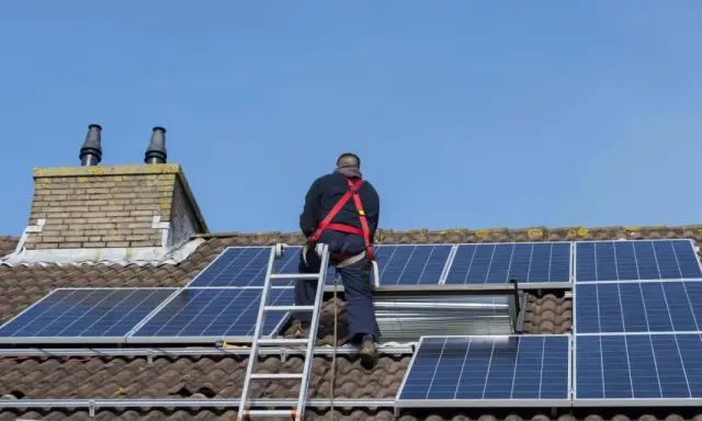 Un homme en harnais installe des panneaux solaires sur un toit. Un projet de panneau solaire installer soi-même en cours.