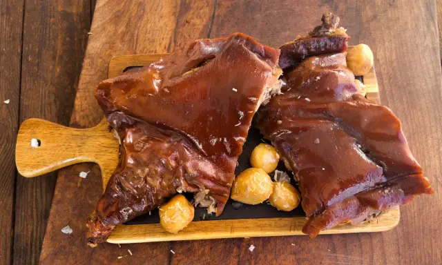Delicioso cochinillo al horno, crujiente y jugoso, servido con patatas asadas sobre tabla de madera.