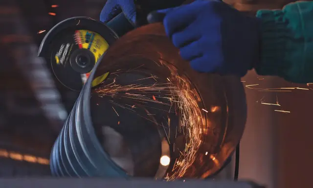 Manos enguantadas usan una radial para cortar un tubo, generando chispas. Un accidente con radial es un riesgo constante.
