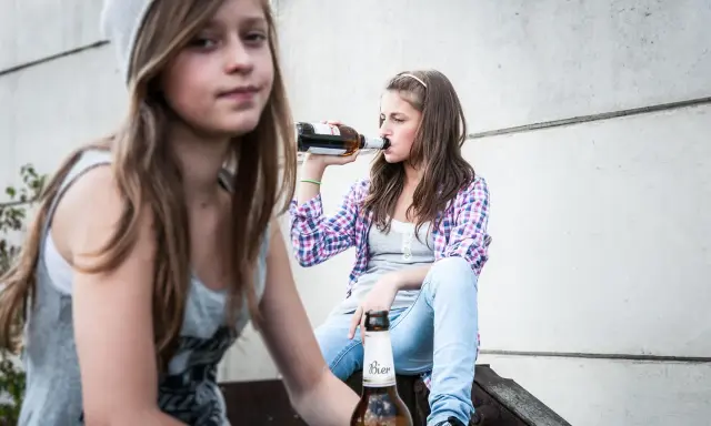 Dwie nastolatki piją piwo, co może być początkiem alkoholizmu wśród młodzieży.
