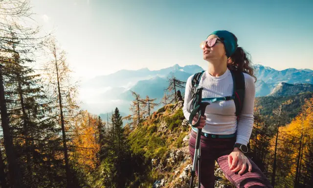Kobieta w sportowym outfit w górach, z kijkami trekkingowymi, podziwia jesienny krajobraz.