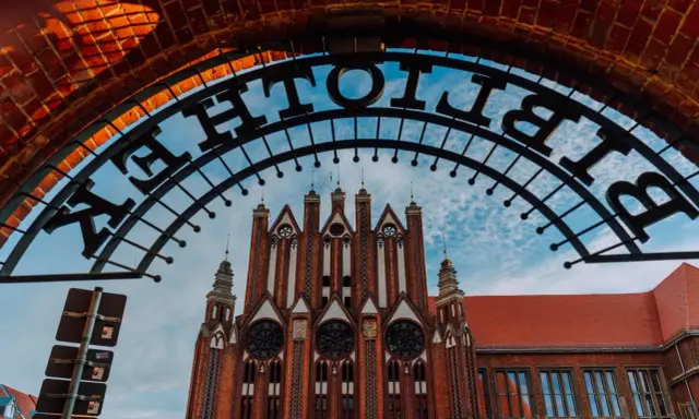 Brama z napisem "Bibliothek" prowadzi do ceglanego budynku w stylu neogotyckim we Frankfurcie nad Odrą.