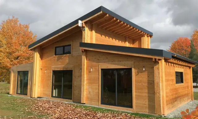 Une belle maison en bois, prête à accueillir ses habitants. L'automne arrive, les feuilles tombent autour de cette construction chaleureuse.