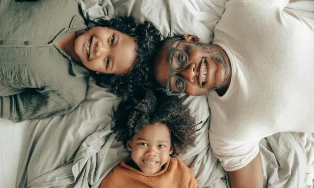Un padre e i suoi due figli sorridono sdraiati sul letto, creando delle foto di famiglia originali e piene d'amore.