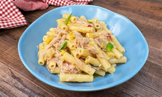Piatto di pasta tonno e limone, condita con tonno sfilacciato, scorza di limone e basilico fresco, servita in un piatto blu.