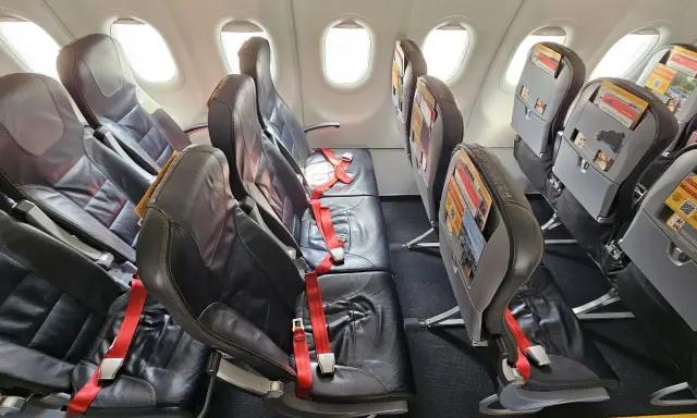 Puste fotele w samolocie Pegasus Airlines, gotowe na odprawę pasażerów. Czerwone pasy bezpieczeństwa czekają.