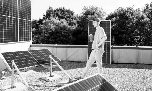 Mann mit Tablet inspiziert Solarmodule auf einem Dach. Der PV-Zubau in Deutschland schreitet voran.