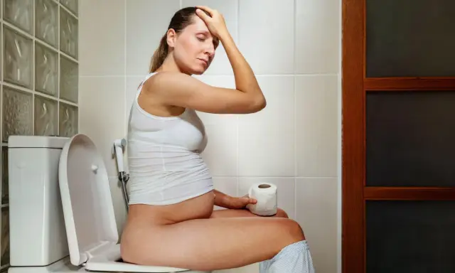 Donna incinta sul water, con la mano sulla fronte, preoccupata per la cacca in gravidanza.