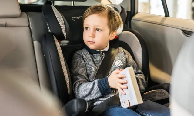 Chłopiec w foteliku samochodowym, jednym z wielu rodzajów fotelików, czyta książkę.