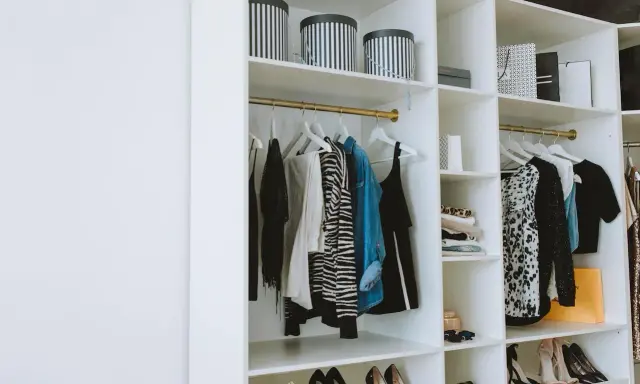 Un armario organizado con ropa colgada y doblada, cajas a rayas y bolsas de compras. Una guía visual de como organizar un armario de forma elegante.