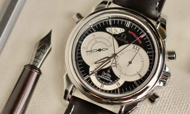 Elegante cronografo rattrapante Omega De Ville con quadrante nero e contatori argentati, accanto a una penna stilografica.