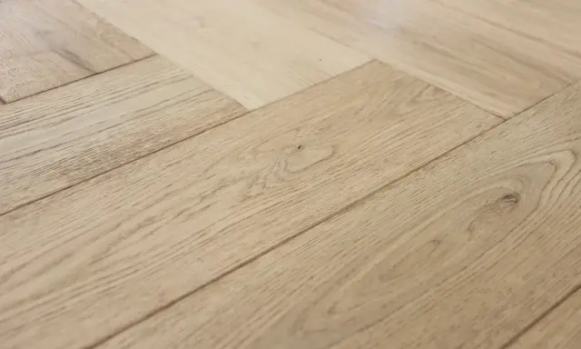 Jasne, drewniane deski ułożone we wzór jodełki francuskiej tworzą elegancką podłogę.