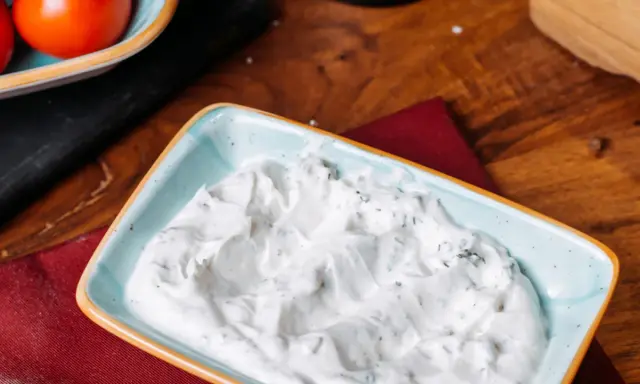 Sauce roquefort crémeuse et onctueuse, parsemée d'herbes vertes, dans un plat bleu clair. Parfait pour accompagner vos plats.