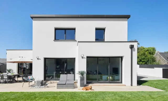 Maison moderne avec jardin, terrasse et chien. La ptz construction maison est visible sous un ciel bleu éclatant.