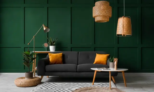 Canapé gris avec coussins orange vif sur fond vert foncé. Le jaune moutarde est une couleur qui va avec le vert foncé, créant un contraste chaleureux.