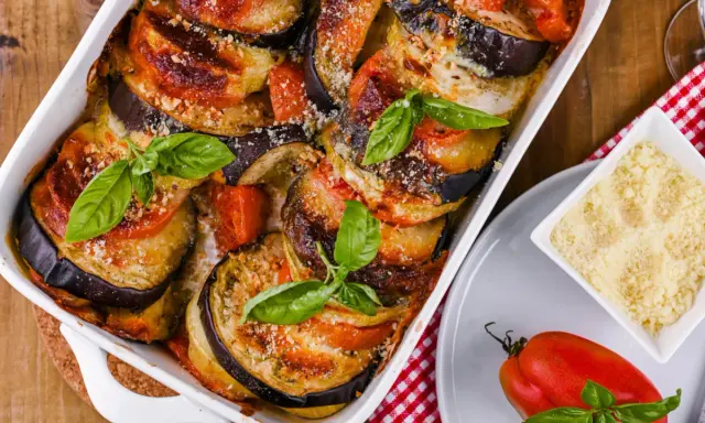 Gebackene Auberginen-Tomaten-Schichten in Auflaufform, garniert mit Basilikum. Perfekt, um Auberginen haltbar zu machen und köstlich zu genießen.