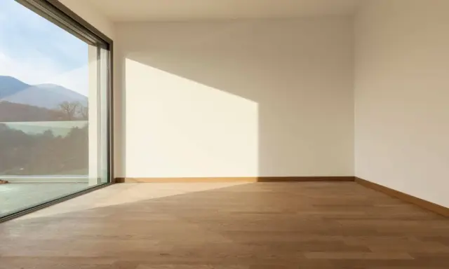 Habitación vacía con suelo de madera y gran ventanal de cristal planitherm que ofrece vistas a montañas.